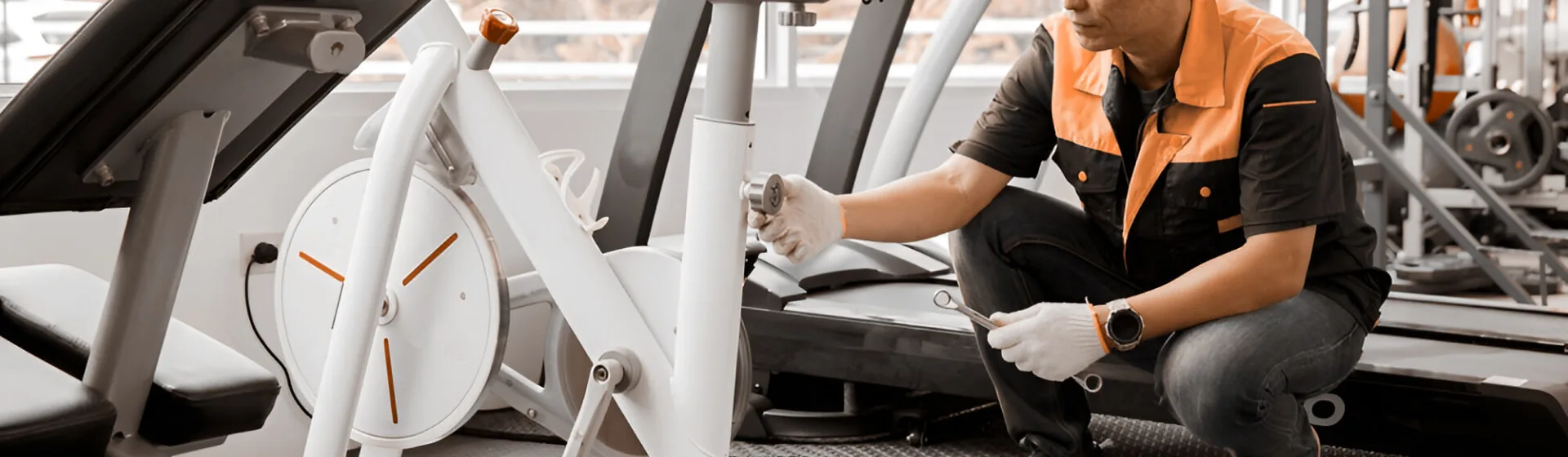 Technician in work gloves servicing a treadmill beside an exercise bike