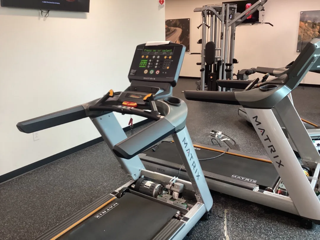 Matrix treadmills in a corporate fitness center, one with its motor hood off for service