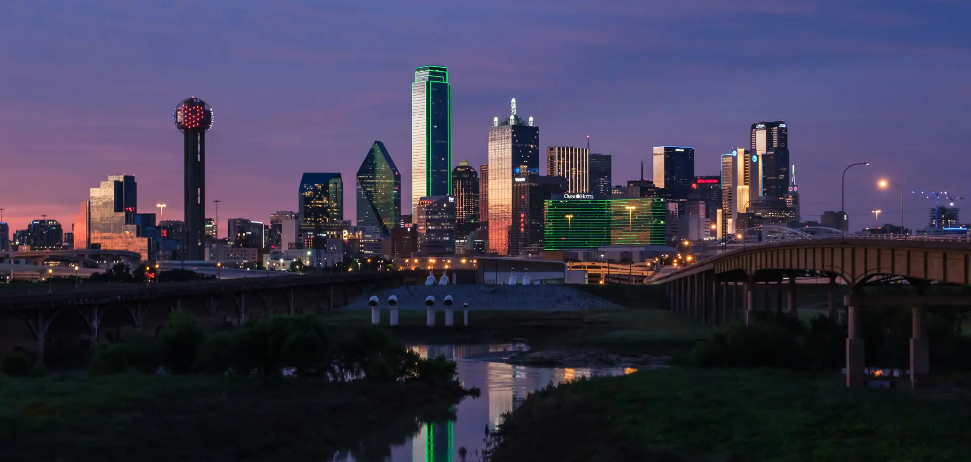 Downtown Dallas skyline at dusk seen across the Trinity River, with Reunion Tower on the left